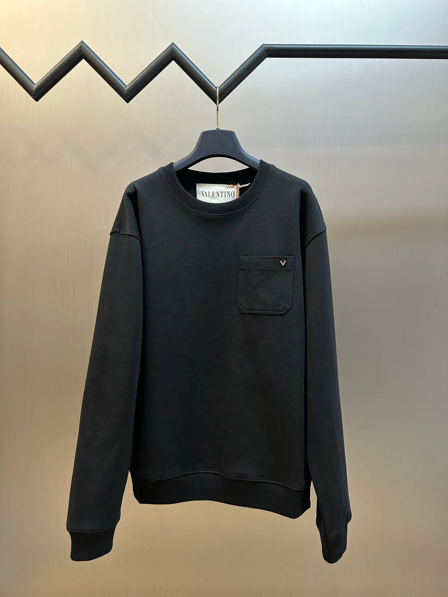 VT logo metal sweatshirt is made of custom-made gilded soft velvet cotton, with a mist-dyed charcoal ink background. The soft light of the night is woven into the cotton velvet, showing the quiet and noble aesthetics of luxury. Classic round neck pullover silhouette. The one-sided patch pocket on the chest is concise and elegant, and the gilded micro V Logo on the pocket is the finishing touch, showing Vt's exclusive luxury charm in minimalism. Manual infrared line drawing pockets use infrared technology as an aid to achieve precise positioning and marking of pocket positions, which retains the precision and flexibility of hand sewing. size：s m l xl